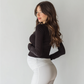 Pregnant woman wearing white maternity leggings with ruched detail and black long sleeve top standing sideways against neutral background