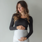 Pregnant woman wearing supportive soft maternity leggings with a full belly panel in white, posing with hands on belly.